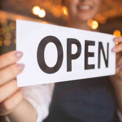 Hands of young waiter or owner of restaurant or cafe putting notice open on the door at the beginning of working day